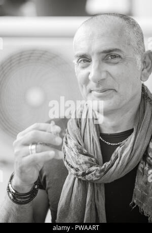 A 50y man is smoking a cigarette. Black and white. The fan coil of an air-conditioner is on the background. Stock Photo
