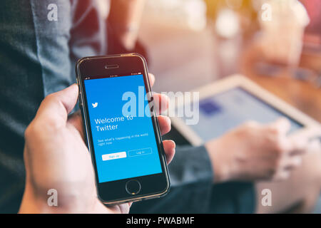 Twitter App on iPhone with people using tablet background closeup male hand hold social network on smart device concept.23 September 2018,Bangkok Thai Stock Photo