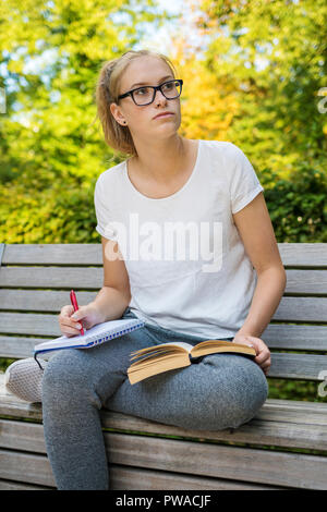Young woman is sitting on a bench and is learning during looking beside Stock Photo