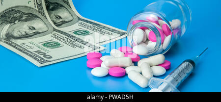 Syringe, dollars and pink and white pills on a bright blue background. Stock Photo