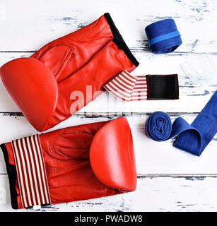 pair of leather red boxing gloves, blue bandage and silicone mouth cap on a white wooden background, top view Stock Photo