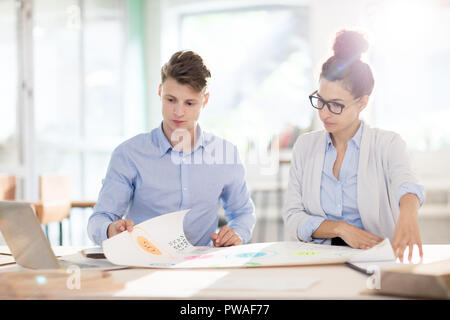 Two young modern engineers in formalwear working with blueprint and analyzing data at meeting Stock Photo