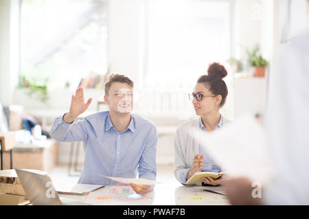 Happy young engineer or expert voicing his ideas while colleague writing them down at meeting Stock Photo