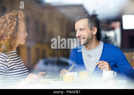 Two colleagues in casualwear sitting in cafe, discussing news and having breakfast or lunch Stock Photo