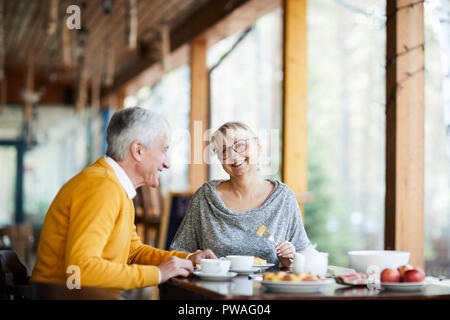 Happy blonde mature female talking to her husband while both having lunch in cafe Stock Photo