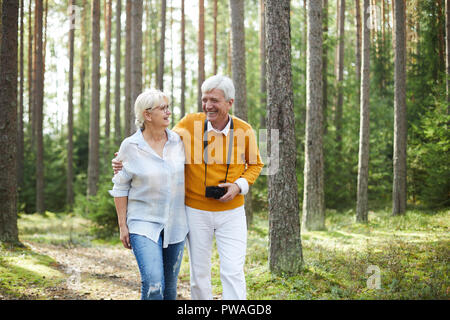 Laughing senior couple taking walk in the forest on summer day, talking and enjoying their chill Stock Photo