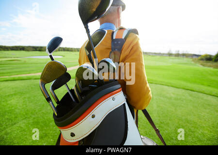 Bunch of golf clubs in bag on shoulder of professional player moving along large green field Stock Photo