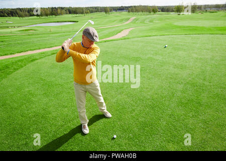 Senior man with golf club ready to hit ball lying on green grass during leisure game Stock Photo