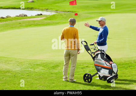 Two active senior man discussing small pond on play field while one of them pointing at it Stock Photo
