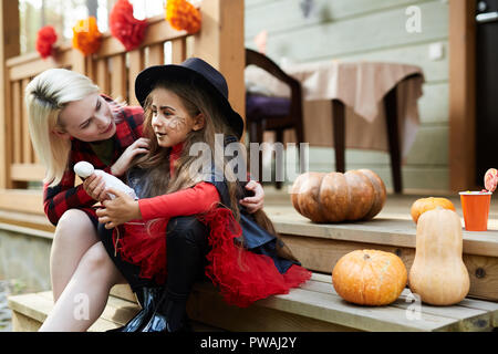 Young mother embracing her little girl in halloween attire while both sitting by terrace of country house Stock Photo