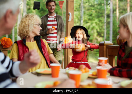 Cute little girl showing her parents and grandparents symbol of halloween by festive dinner in the country Stock Photo