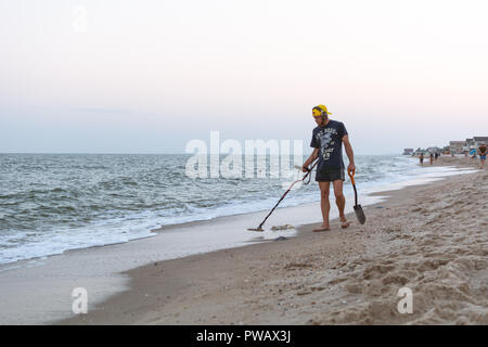 Treasure hunter with a metal detector walks along the beach of the Black Sea after sunset looking for treasure Stock Photo