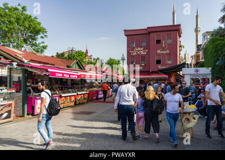 Various stalls selling Kumpir or baked potatoes line a cobbled street as people walk past in the Ortaköy district, Istanbul, Turkey Stock Photo