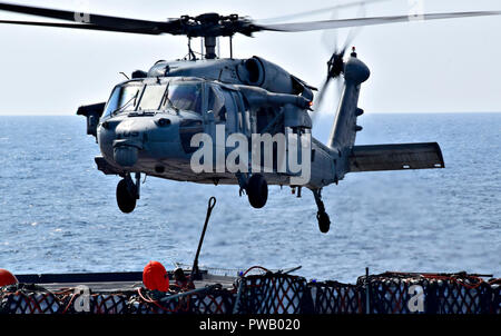 PHILIPPINE SEA (Oct. 10, 2018) - A flight deck crew member aboard the dry cargo and ammunition ship USNS Wally Schirra (T-AKE 8) attaches a cargo hook to an MH-60S Sea Hawk helicopter, assigned to the 'Island Knights' of Helicopter Sea Combat Squadron (HSC) 25  during a vertical replenishment with the amphibious assault ship USS Wasp (LHD 1). Wasp, flagship of Wasp Amphibious Ready Group, with embarked 31st Marine Expeditionary Unit, is operating in the Indo-Pacific region to enhance interoperability with partners and serve as a ready-response force for any type of contingency. (U.S. Navy phot Stock Photo