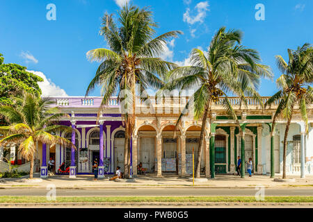 Old Spanish colonial colorful houses with palms in the foreground, across the street in the center of Cienfuegos, Cuba Stock Photo