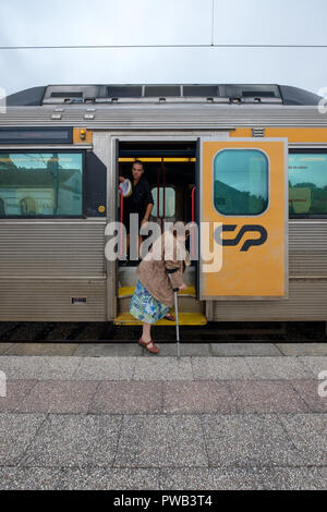 Old woman using a crutch getting off a train Stock Photo