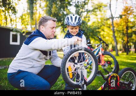 Father's day Caucasian dad and 5 year old son in the backyard near the house on the green grass on the lawn repairing a bicycle, pumping a bicycle whe Stock Photo