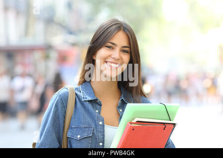 Happy student holding folders poses looking at camera in the street Stock Photo