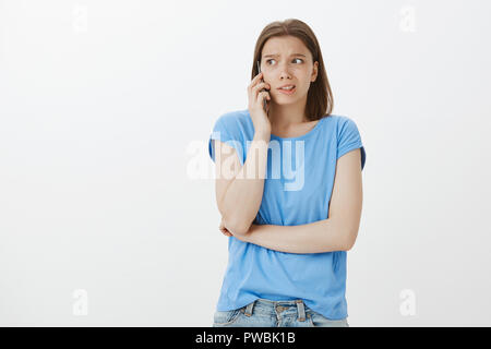 Anxious female student calling angry teacher to apologize for not comming to exam. Nervous timid woman in casual outfit, holding hand crossed on chest, calling on smartphone, intense and scared Stock Photo