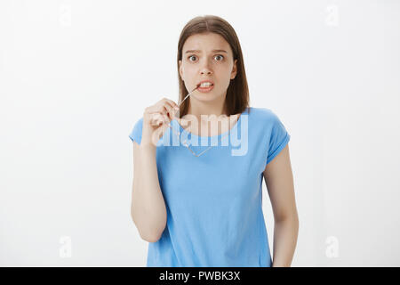 worried anxious girl with fair hair wearing blue t shirt biting rum of glasses and staring nervous at camera looking with popped eyes feeling scared while waiting for important results
