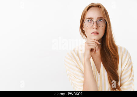 Woman remembering schedule while planning next work day standing focused and perplexed in trendy glasses looking at upper left corner thoughtful and concentrated making calculations in mind Stock Photo