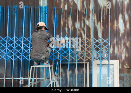 Vietnamese worker painting a fence in Blue, Hoi An, Vietnam Stock Photo