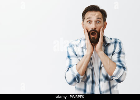 Oh no, new wrinkles. Portrait of shocked upset good-looking mature guy looking at camera as if in mirror, dropping jaw and popping eyes from astonishment, touching face nervously with palms Stock Photo