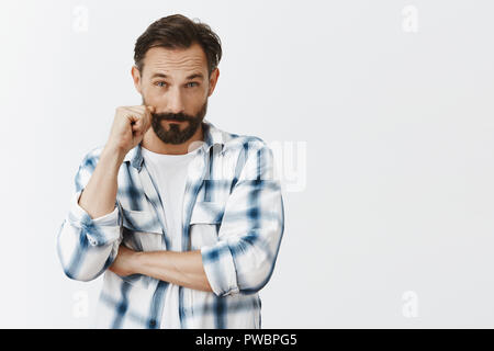 Father looking suspiciously at son who came late, making strange accuses. Dubtful attractive mature male with beard, touching moustache and staring with disbelief at camera, listening and thinking Stock Photo