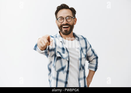 Haha got you. Portrait of carefree funny and emotive handsome mature coworker with beard in checked shirt and glasses, pointing at camera with index finger and laughing over out loud, being rude Stock Photo
