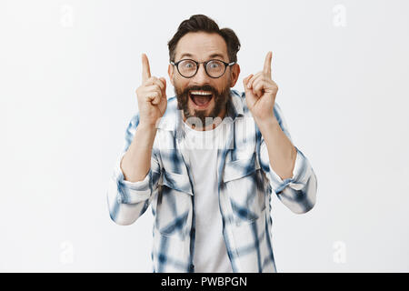 Correct, your are right, excellent point of view. Portrait of charming emotive and thrilled male teacher in glasses, raising both index fingers and being amazed with smart students over grey wall Stock Photo