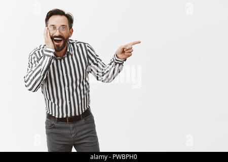 Guy gossiping about classmate with friends during college reunion, laughing over person who gained weight, being surprised and impressed pointing right and bending towards mates while spreading rumors Stock Photo