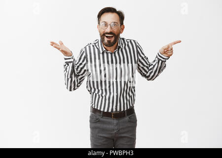 Who could thought. Impressed happy and surprised attractive mature male with beard in glasses and formal shirt, pointing right and shrugging, being interested and thrilled with amazing things Stock Photo