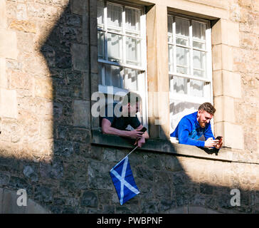 Young men leaning out of windows watching Scottish Independence All under one Banner AUOB march, Royal Mile, Edinburgh, Scotland, UK Stock Photo