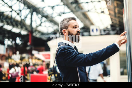 Side view of hipster businessman standing on bus or train station, checking timetable. Stock Photo