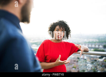 Two businesspeople standing against London rooftop view, leaning on a railing. Stock Photo