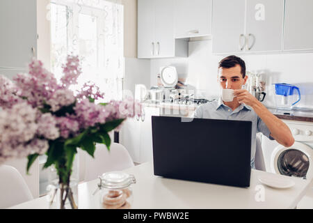 Young businessman using laptop while having coffee in modern kitchen at home. Breakfast of an entrepreneur Stock Photo