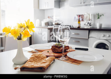 Dinner for two served in kitchen. Modern kitchen design. Roasted meat. Clean kitchen decorated with flowers Stock Photo