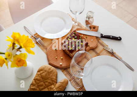 Dinner setting for two served in kitchen. Roasted meat with wine prepared in dining room. Stock Photo
