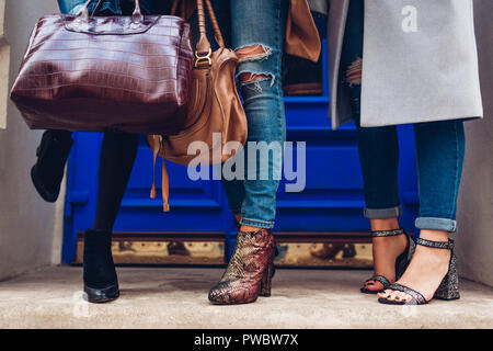 Three women wearing stylish shoes and accessories outdoors. Beauty fashion concept. Ladies holding modern female handbags Stock Photo