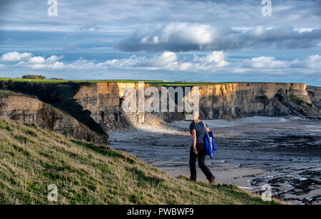 A woman walks along Witches Point overlooking the cliffs at Temple Bay on the Vale of Glamorgan Heritage Coast, South Wales. Stock Photo