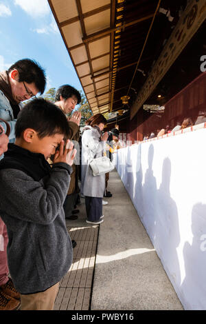 Japanese new year, shogatsu. Child, 6-7 years with People praying at the scared area in the main hall, Honden of the Nishinomiya Shinto shrine. Stock Photo