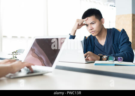 Serious concentrated young Asian programmer focused on work sitting at table and installing setup for laptop in open space Stock Photo