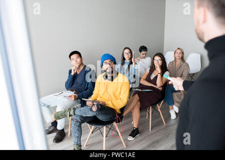 Curious young multi-ethnic students sitting on chairs in auditorium and listening to teacher while studying at training class Stock Photo