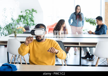 Serious concentrated young middle-eastern man sitting at table in coworking space and working on project while using VR headset Stock Photo