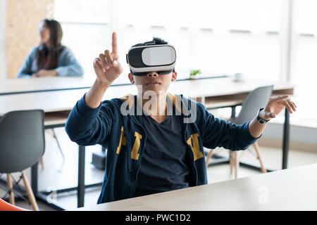 Content curious modern Asian guy sitting at table and using invisible screen while testing new virtual reality app in open space office Stock Photo