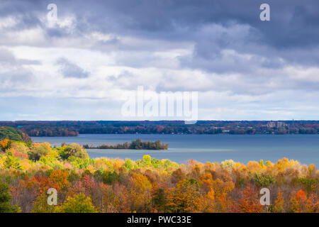 Sun breaking through the clouds appears to set the fall foliage ablaze near Lake Couchiching Orillia Ontario Canada. Stock Photo