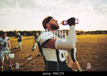 American football player drinking water from a bottle while standing on a field during a team practice Stock Photo