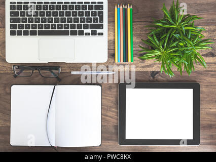 notepad, laptop, green plant and tablet computer on wooden desk Stock Photo