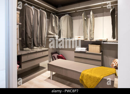 Interior of a walk in closet with hanging clothes and built in drawer units and seating in a luxury modern home Stock Photo