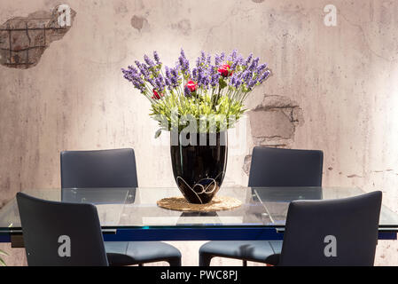 Dining table with floral centerpiece with colorful blue and red flowers in a vase and a textured grey background wall Stock Photo